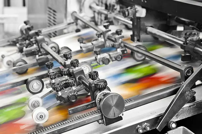 A photo of a press run of a commercial printer shows printed items moving quickly through an industrial printer